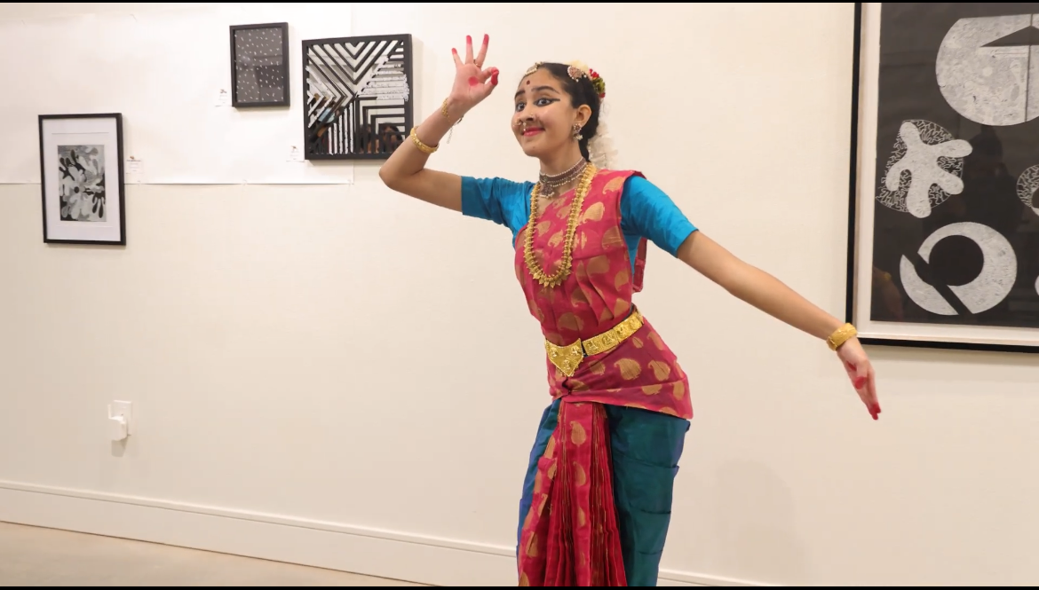 Woman in traditional attire dancing in a room with framed pictures on the wall.